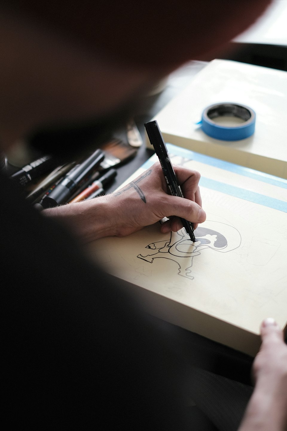 Artist drawing character design with black marker on board.